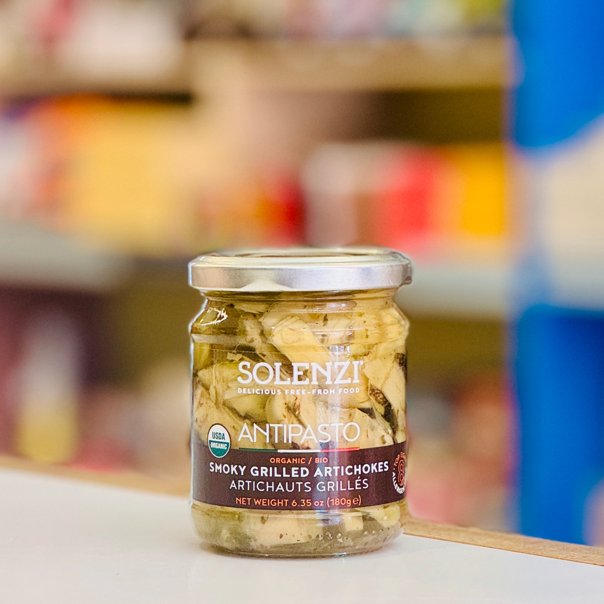 Jar of Solenzi Antipasto smoky grilled artichokes on a shelf with a blurred store background