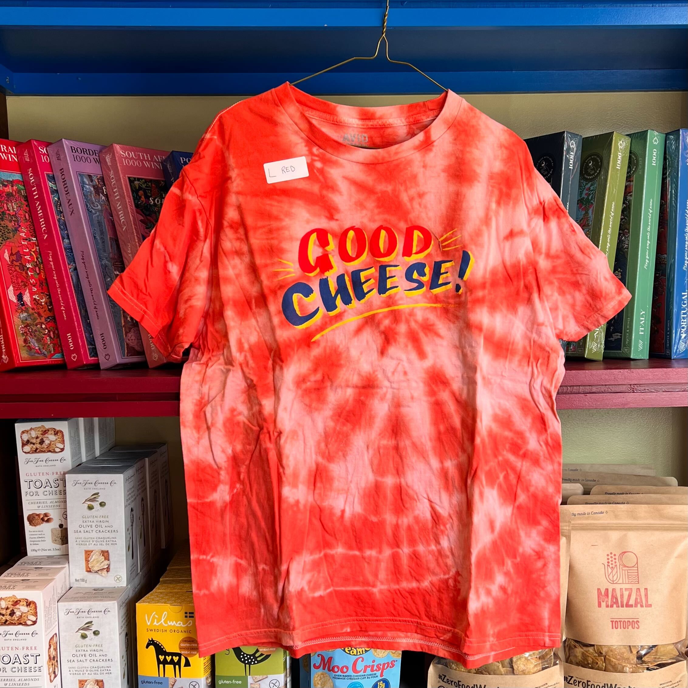 Red tie-dye t-shirt with 'Good Cheese!' text on a hanger against a bookshelf background.