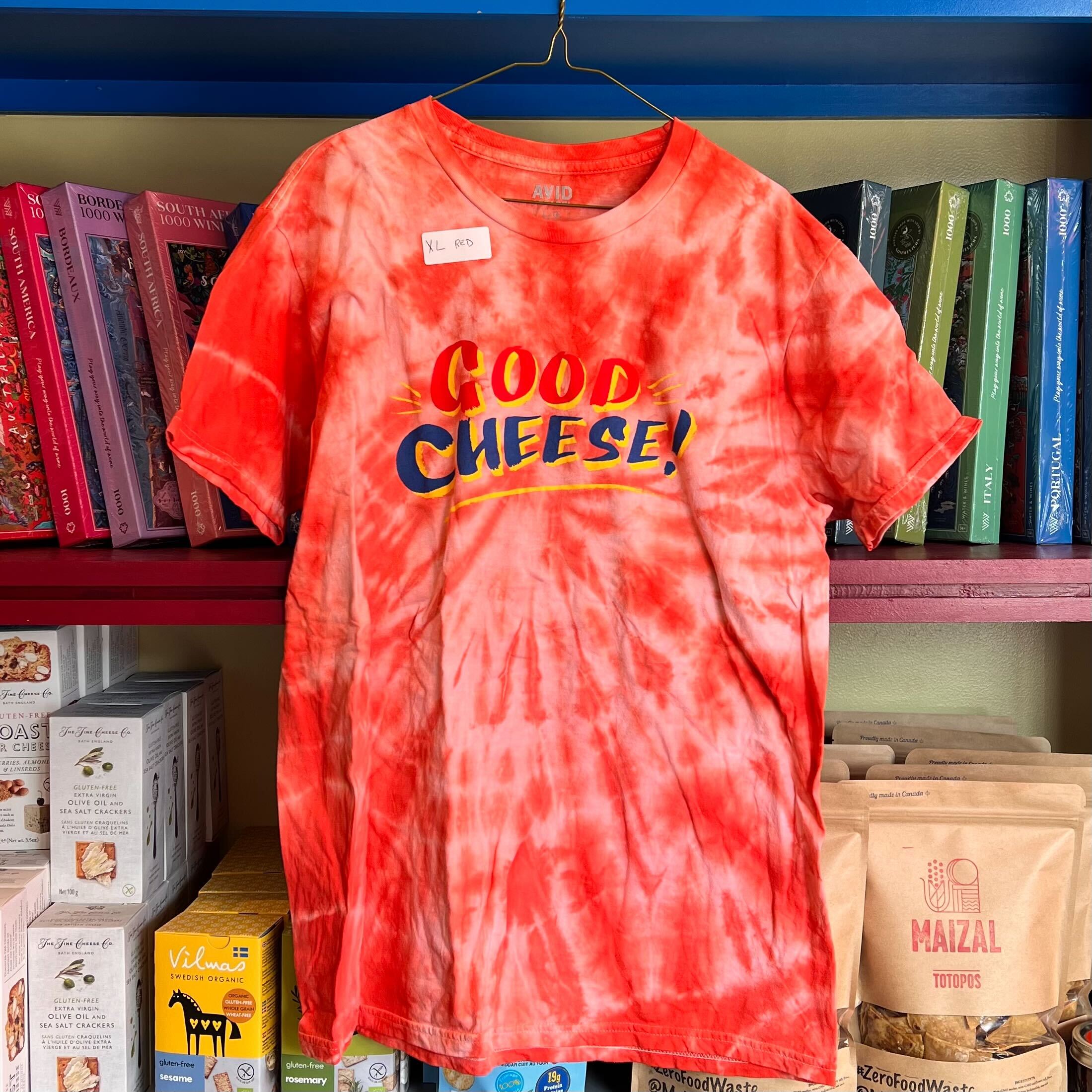 Red tie-dye t-shirt with 'Good Cheese!' text on a hanger against a bookshelf background
