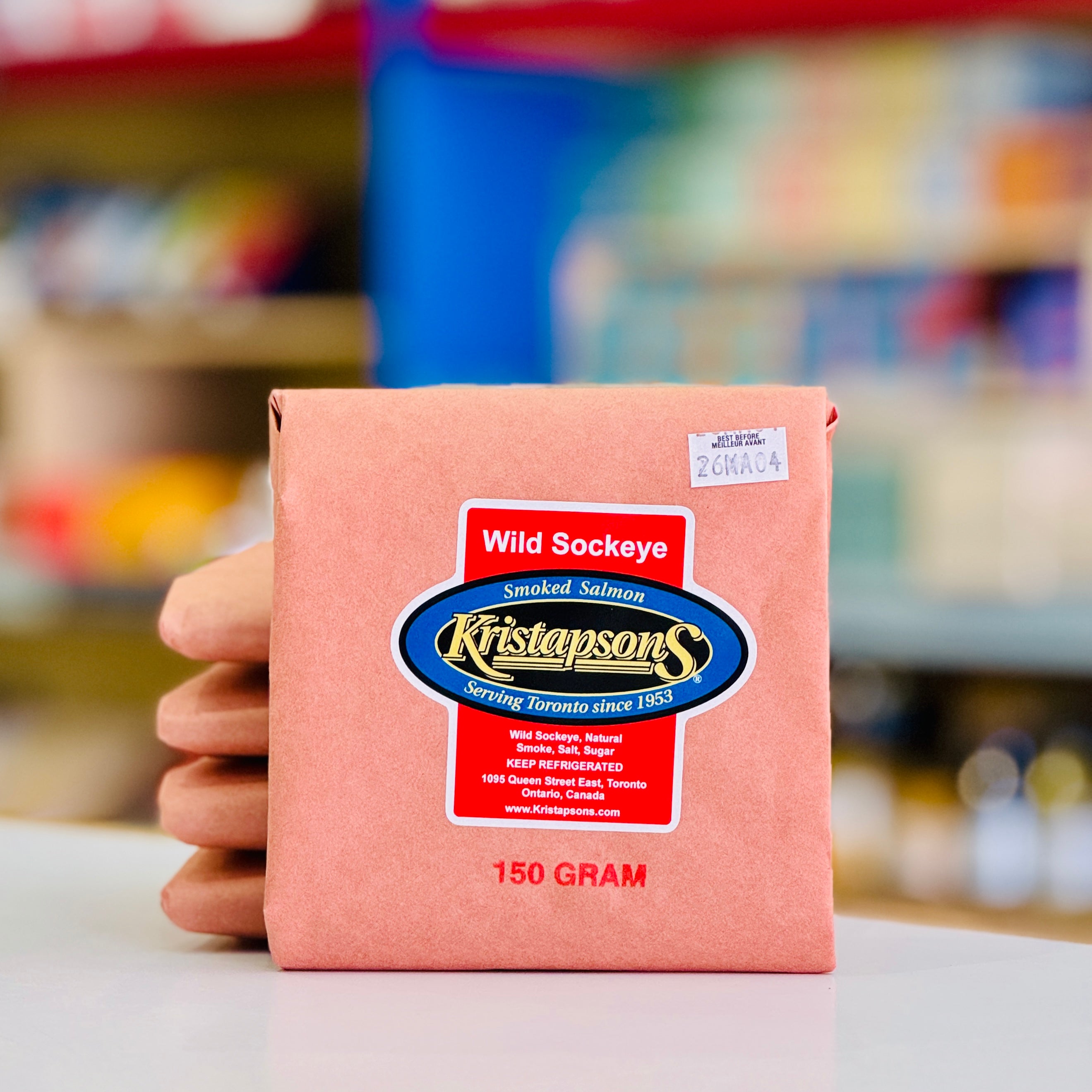 Packaged smoked salmon with Kristapsons label held by a hand in a store setting