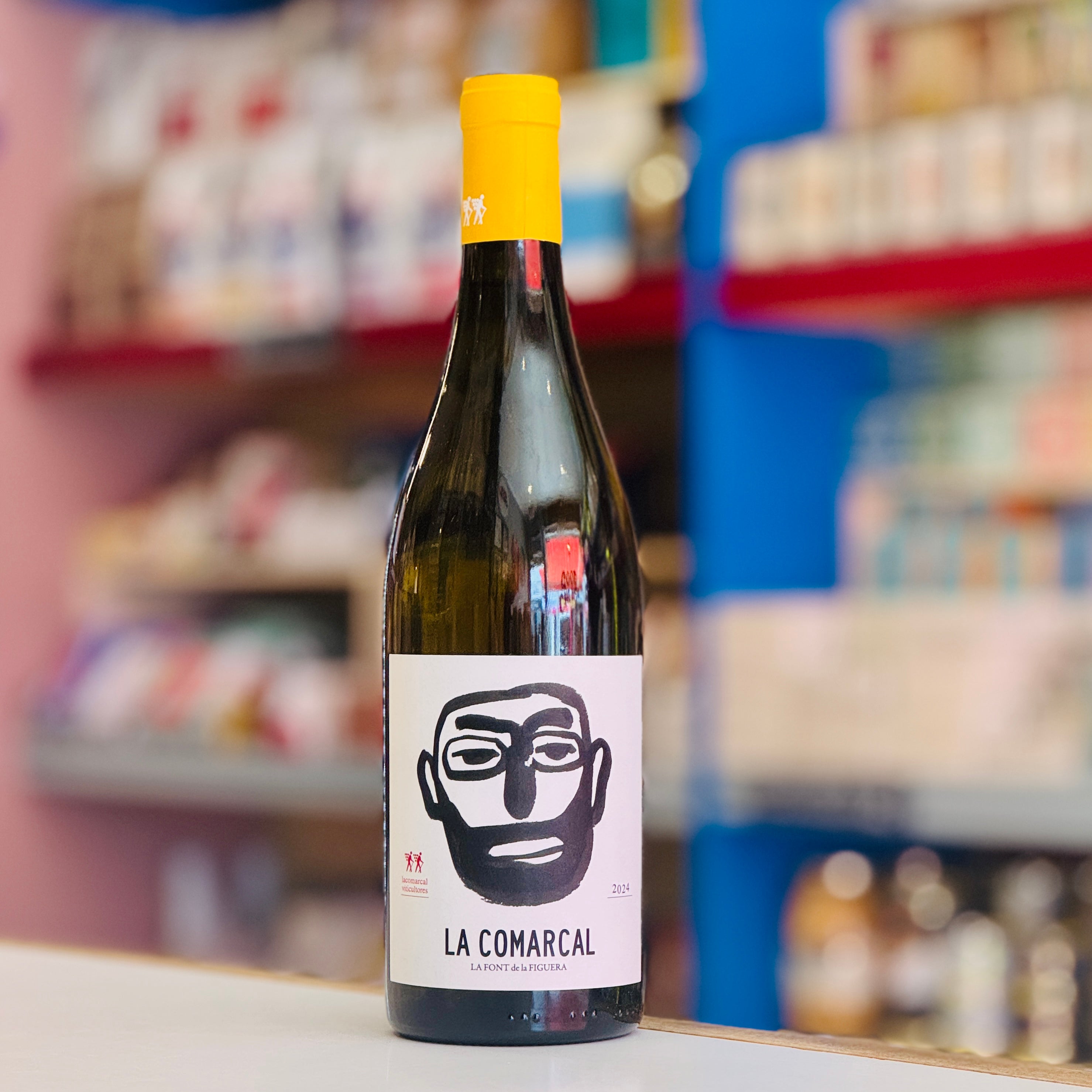 Bottle of La Comarcal wine with a yellow cap on a shelf in a store.